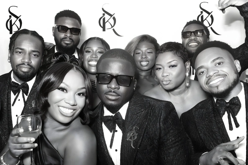 Group of eight men and women dressed formally, smiling and posing closely together in a black and white photo.