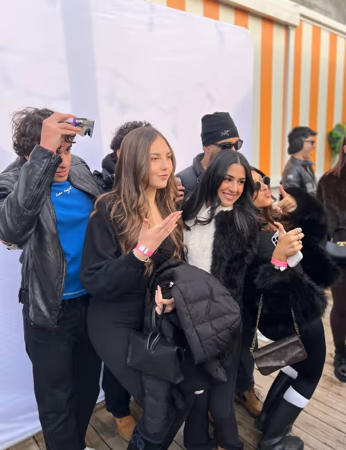 Group of young people posing happily together outdoors, some making hand gestures and smiling.