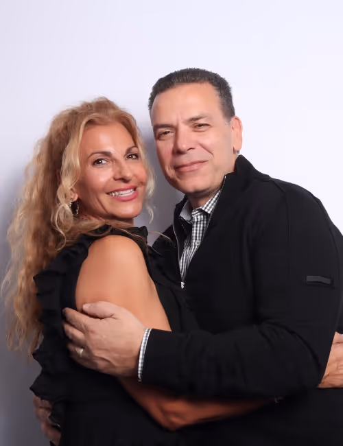 Smiling middle-aged couple embracing against a plain light gray background.