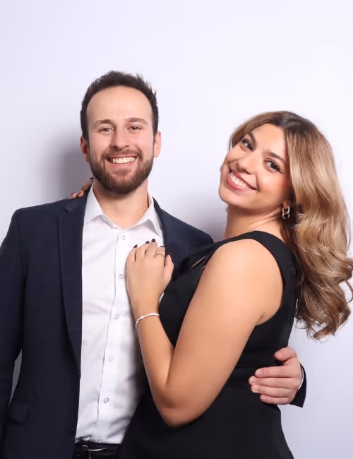 Smiling man in suit and woman in black dress posing together against a plain background.
