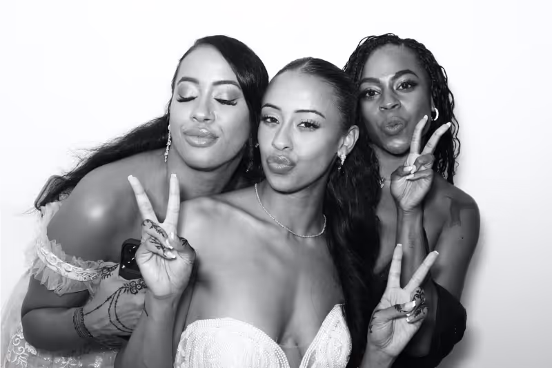 Three women posing closely, making peace signs and duck faces in a black and white photo.