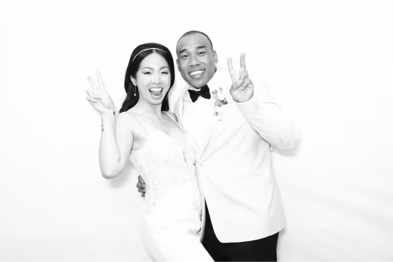 Smiling bride and groom making peace signs and posing closely in a black-and-white photo.