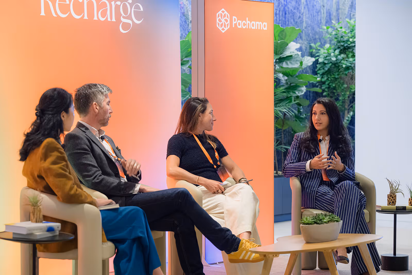 Four people engaged in a panel discussion with Pachama branding on an orange backdrop and plants in the background.
