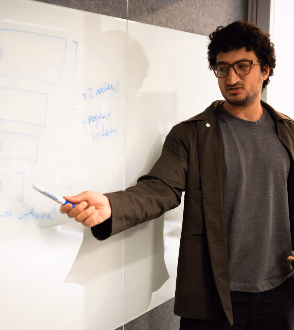Man with salt-and-pepper hair and beard, wearing a dark blazer and white shirt, speaking with hand raised.