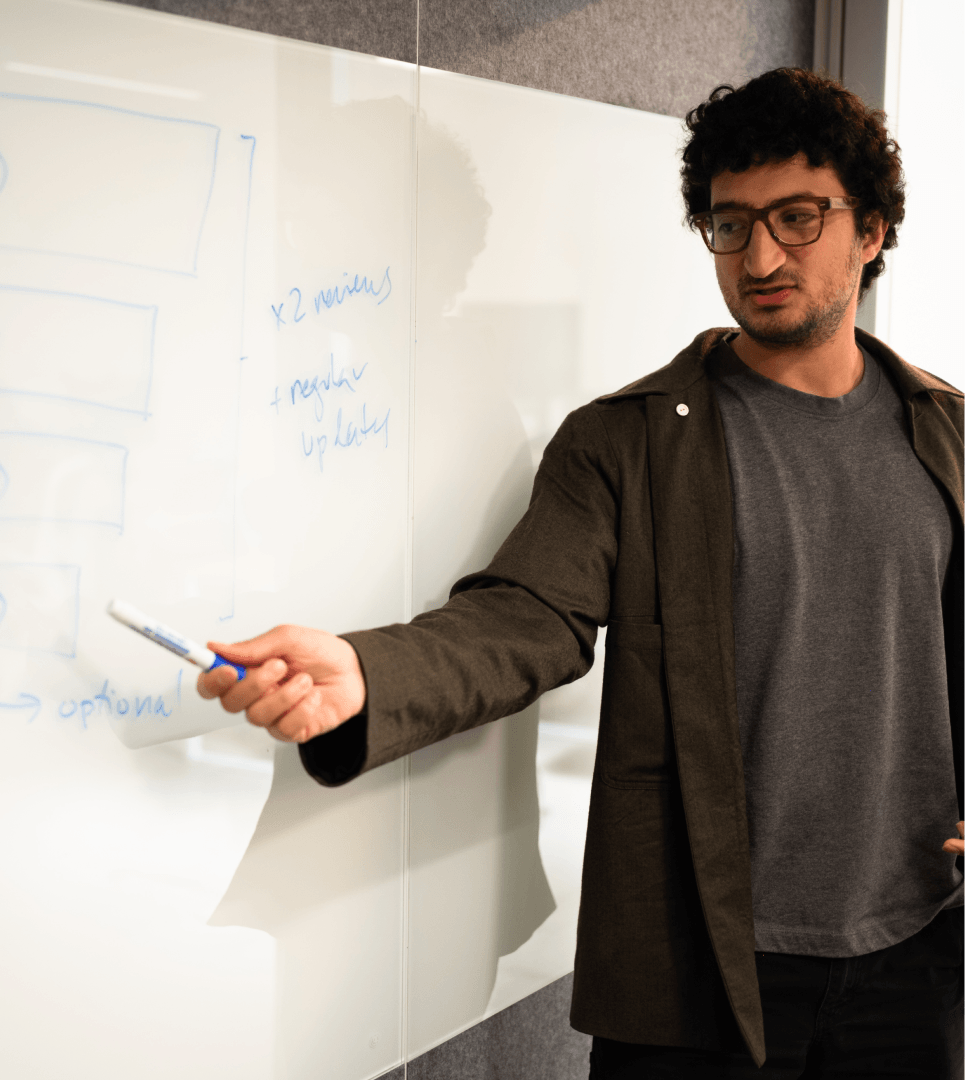 Man with salt-and-pepper hair and beard, wearing a dark blazer and white shirt, speaking with hand raised.