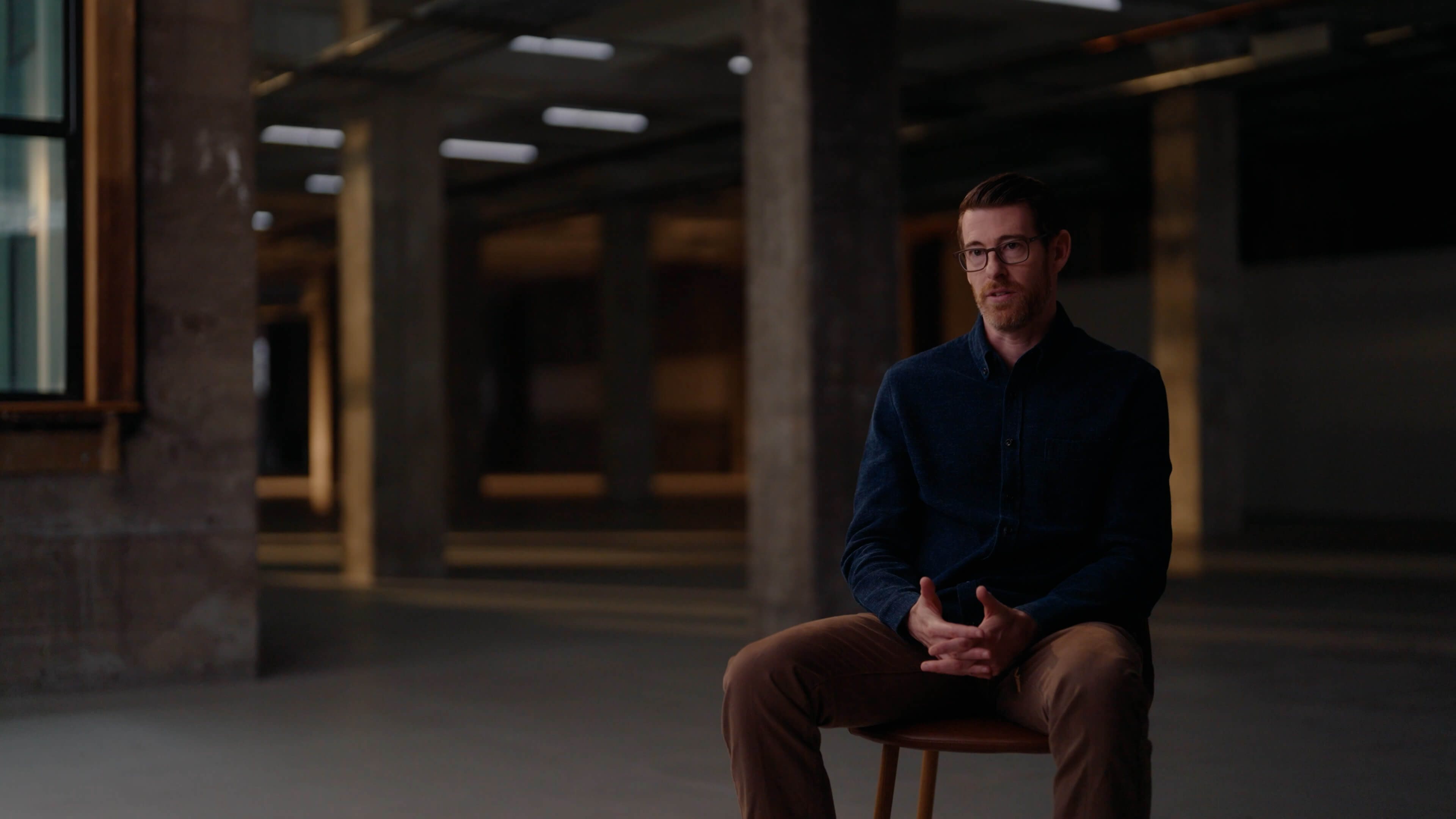 Man with salt-and-pepper hair and beard, wearing a dark blazer and white shirt, speaking with hand raised.
