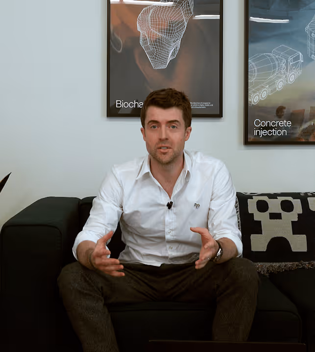 Man with salt-and-pepper hair and beard, wearing a dark blazer and white shirt, speaking with hand raised.
