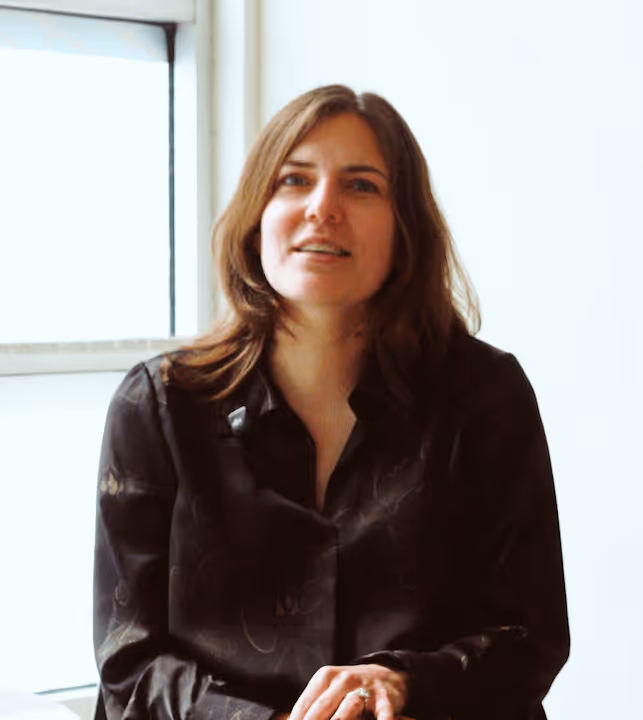 Man with salt-and-pepper hair and beard, wearing a dark blazer and white shirt, speaking with hand raised.