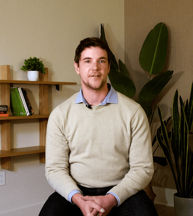 Man with salt-and-pepper hair and beard, wearing a dark blazer and white shirt, speaking with hand raised.