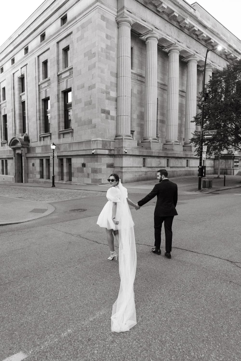 Bride and groom walking across the street with wedding veil blowing in the wind in downtown Montreal