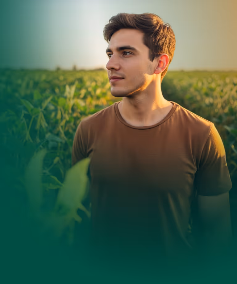 Jovem estudante da graduação olhando para o horizonte em meio a uma grande plantação de soja.
