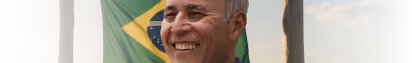 Clóvis sorrindo diante da bandeira do Brasil na campanha Outubro do Produtor