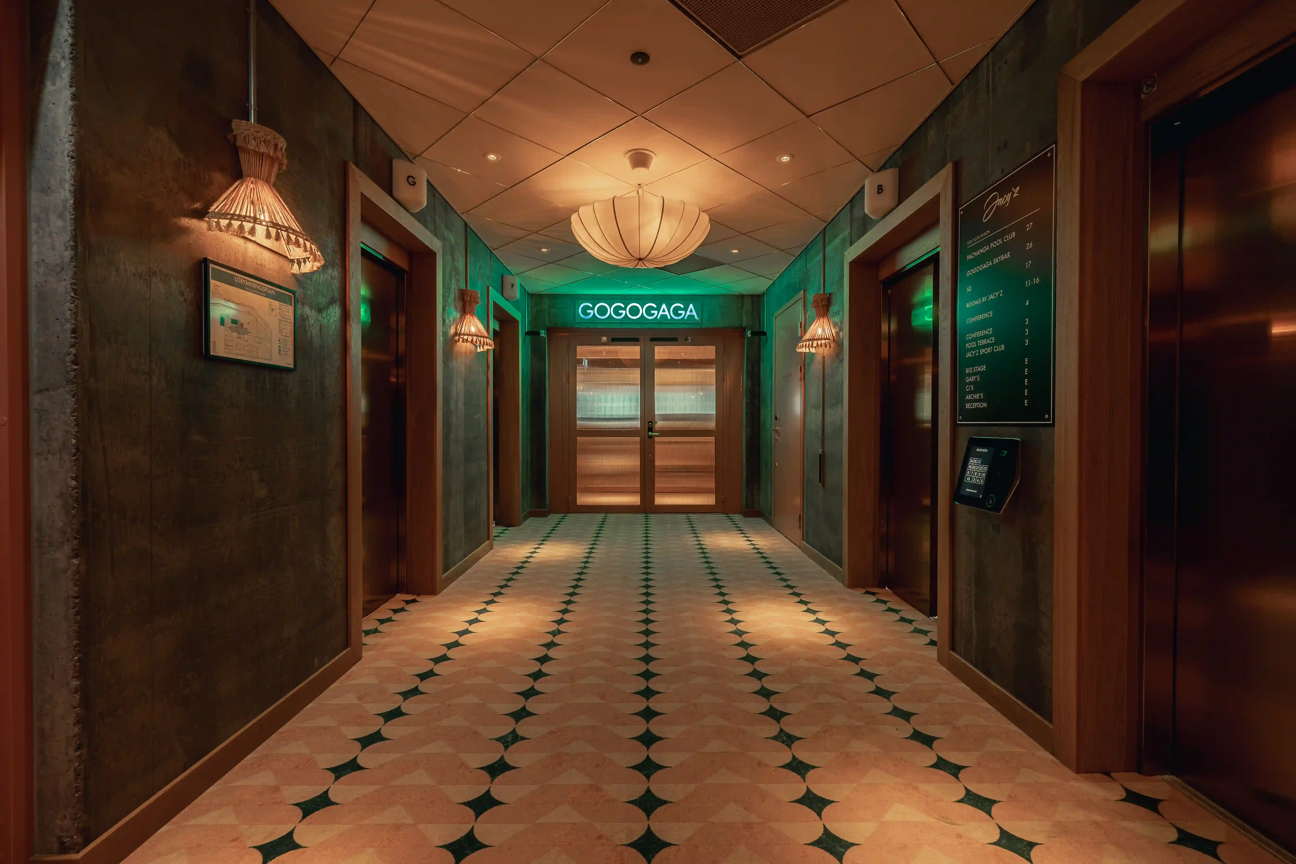 Hall med grön belysning och dekorerade väggar, med en neonskylt som lyder ‘GOGOGAGA’ ovanför dörrarna.