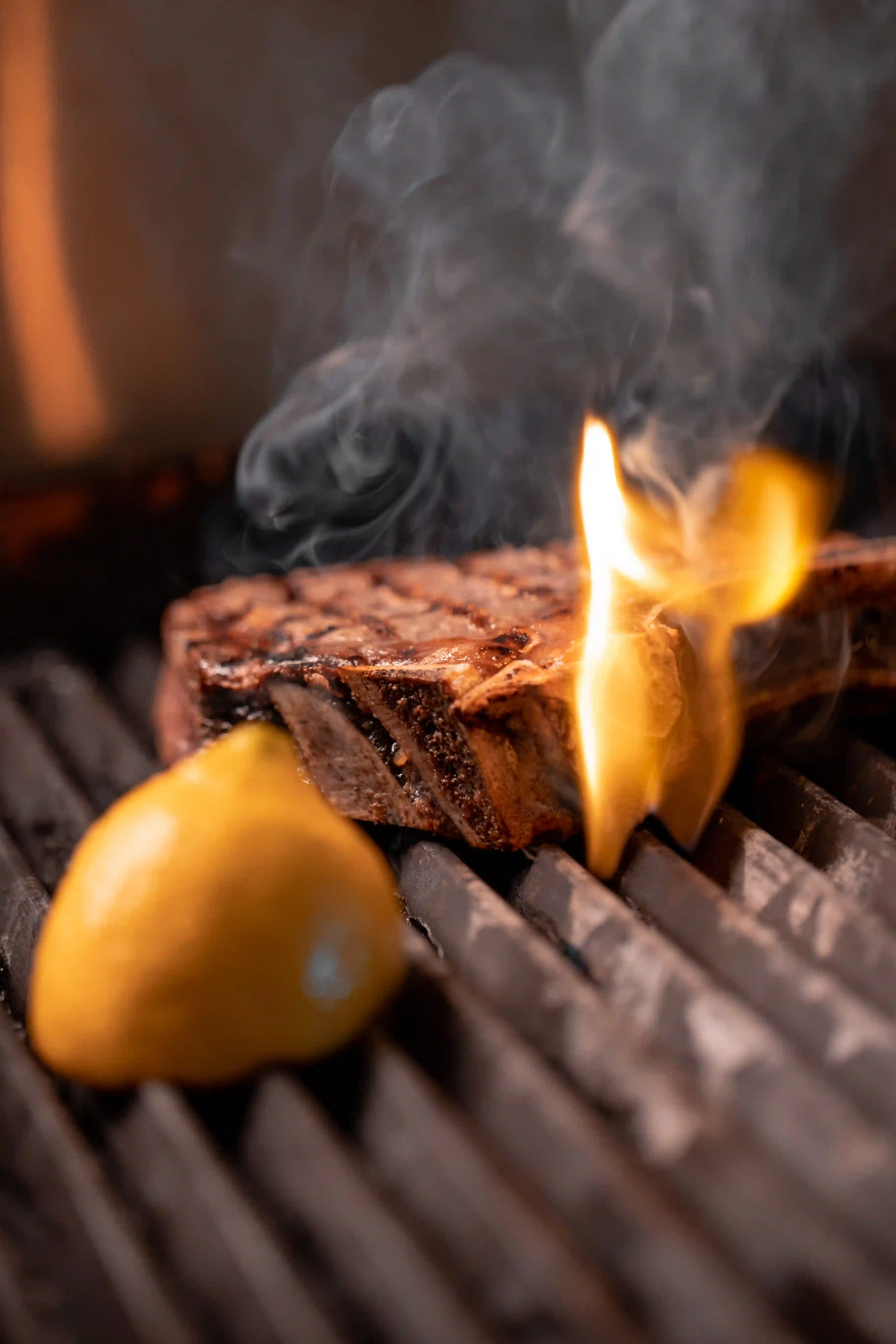 Närbild på en saftig stek som grillas, med en citron bredvid och en flamma som lyser upp köttet