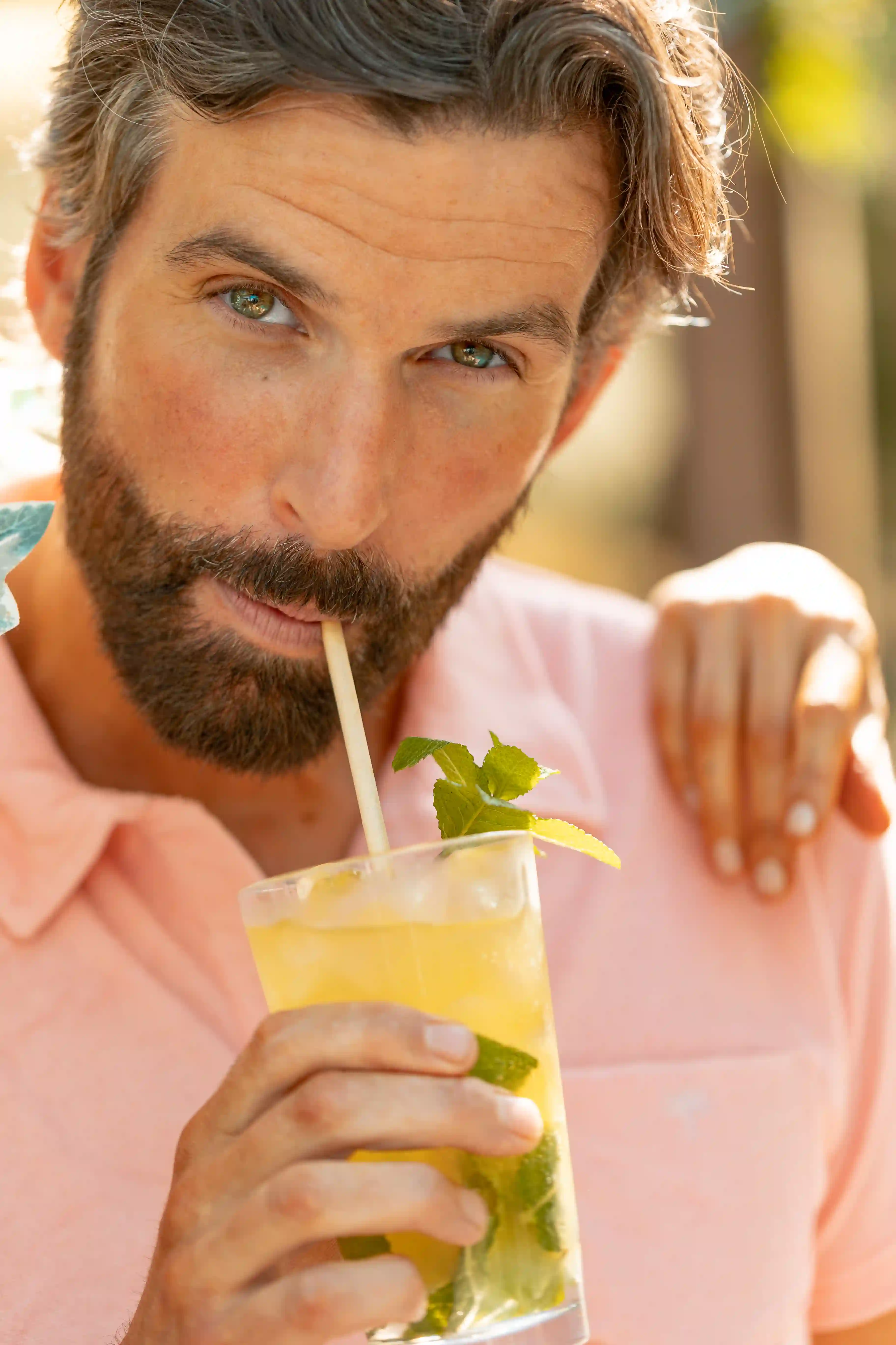 Man i rosa skjorta njuter av en kall drink med mynta och lime, tittar avslappnat in i kameran.