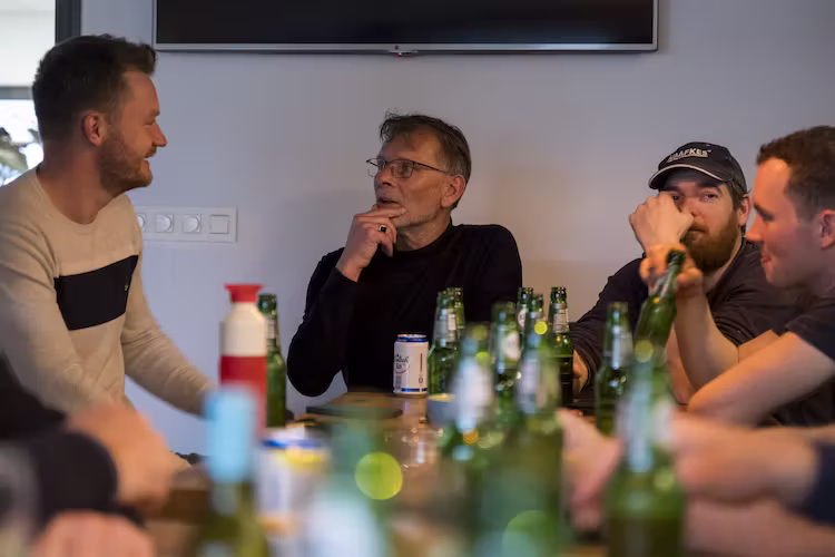 Vier medewerkers van Haafkes zitten rond een tafel vol met bierflessen, praten en lachen tijdens de naborrel.