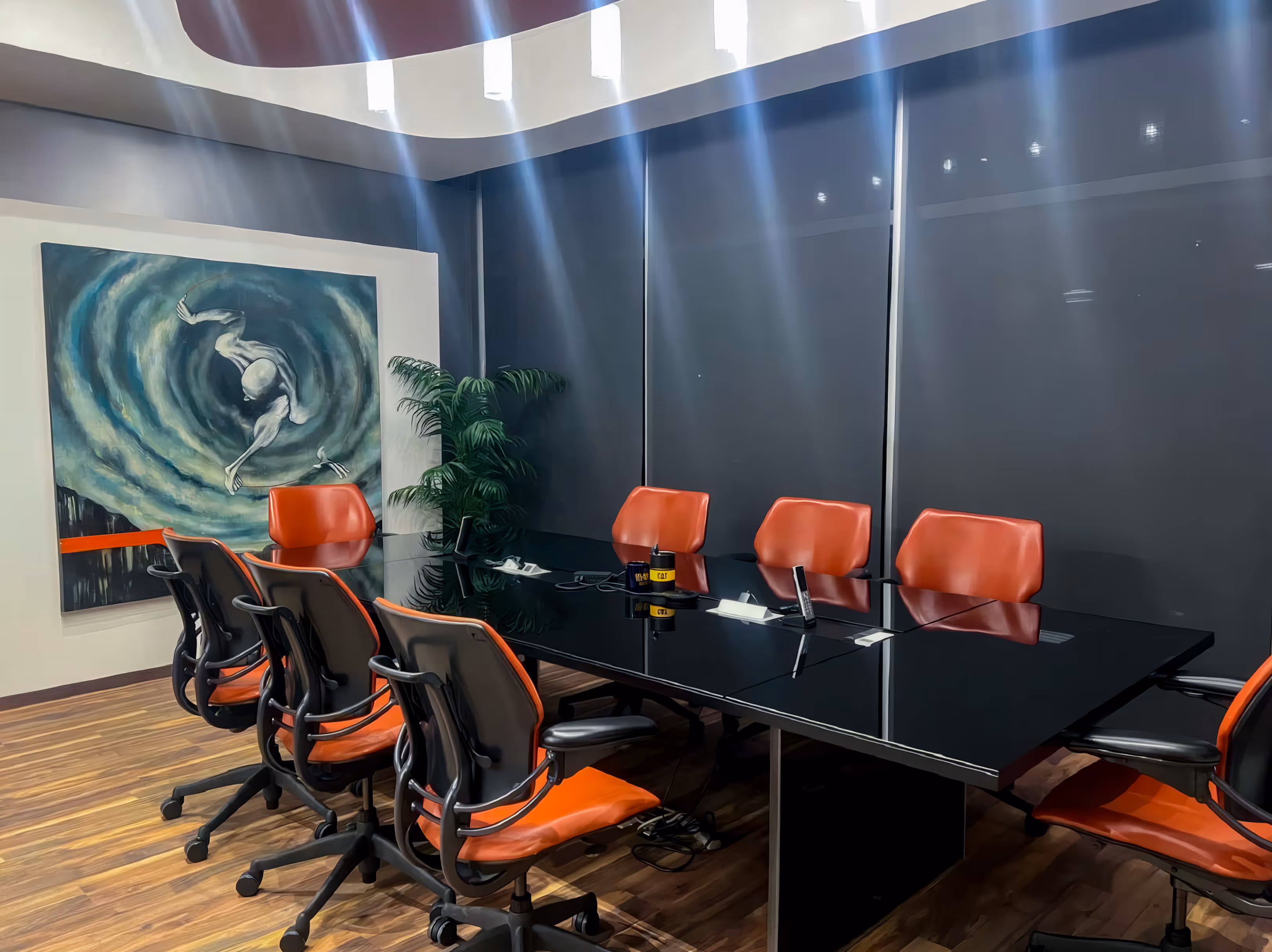 Sala de juntas moderna con una mesa larga de cristal negro, sillas ergonómicas en color naranja y negro, y un cuadro de arte contemporáneo en la pared.