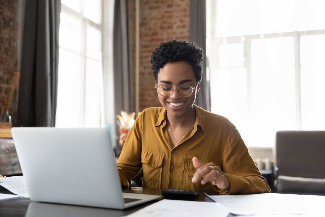 A young woman in glasses doing math on calculator at and budgeting on laptop computer smiling