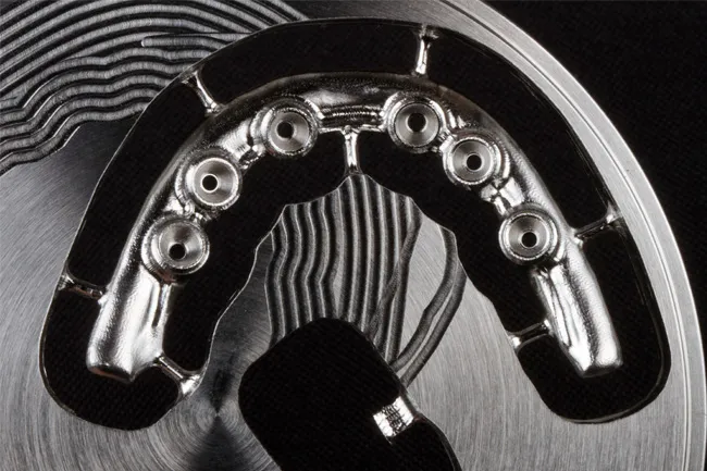 Close-up of a metallic dental implant template with multiple screw holes on a textured background.