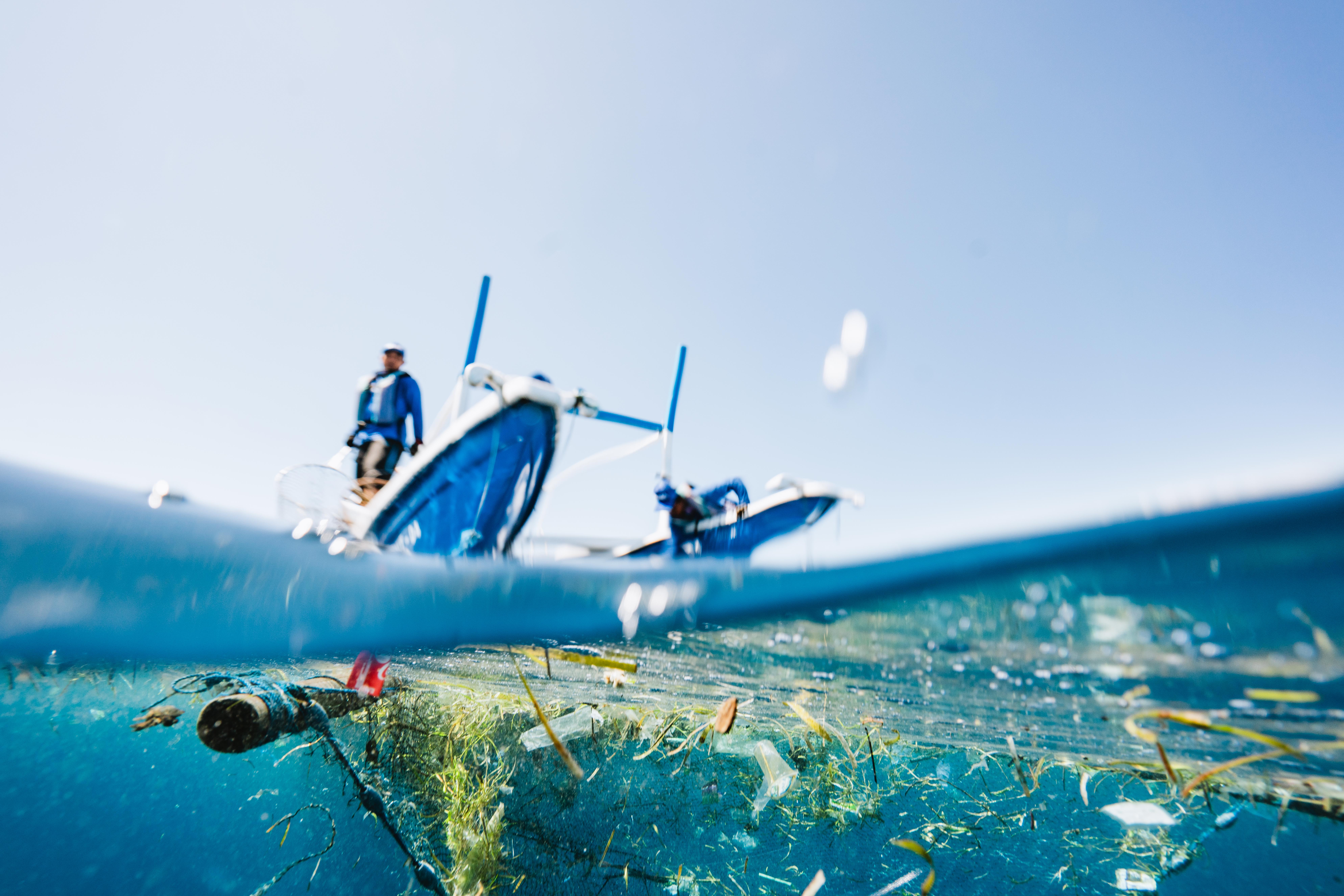Two people on a boat cleaning trash in the ocean.