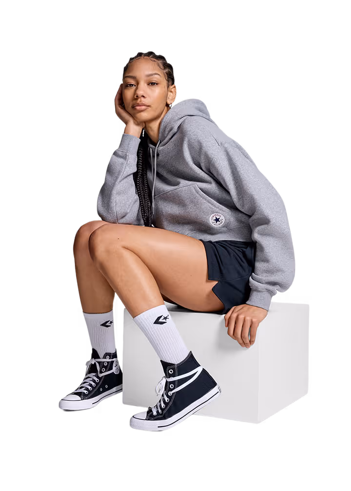 Young woman sitting on a white block wearing a gray hoodie, black shorts, white socks, and black high-top sneakers.