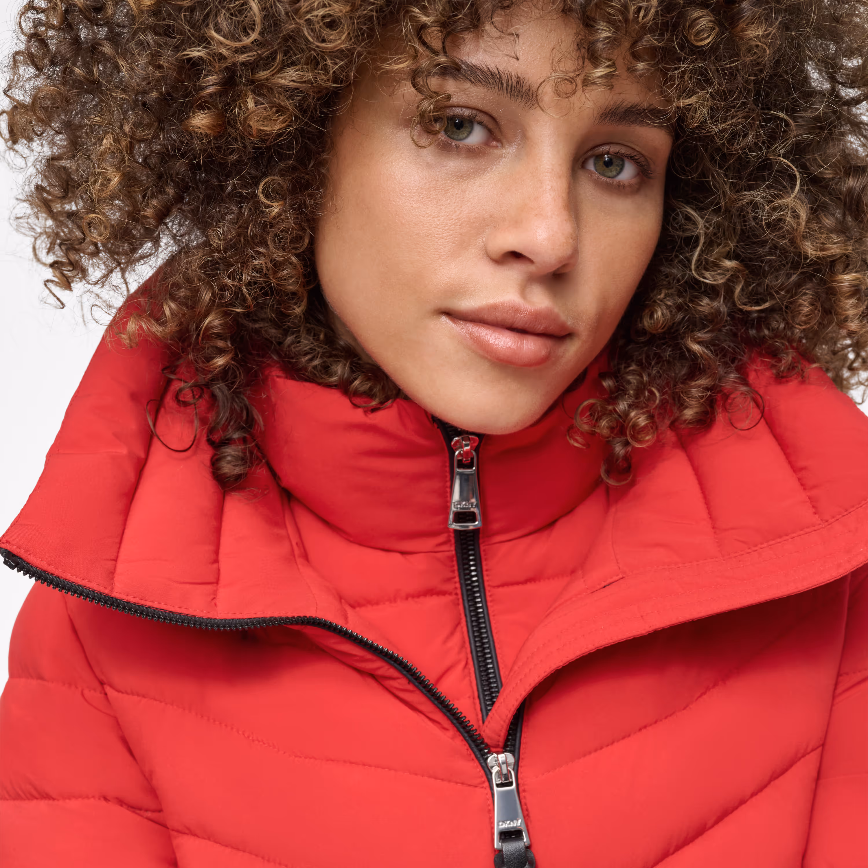 Close-up of a person with curly hair wearing a red puffer jacket with a high collar and zipper.
