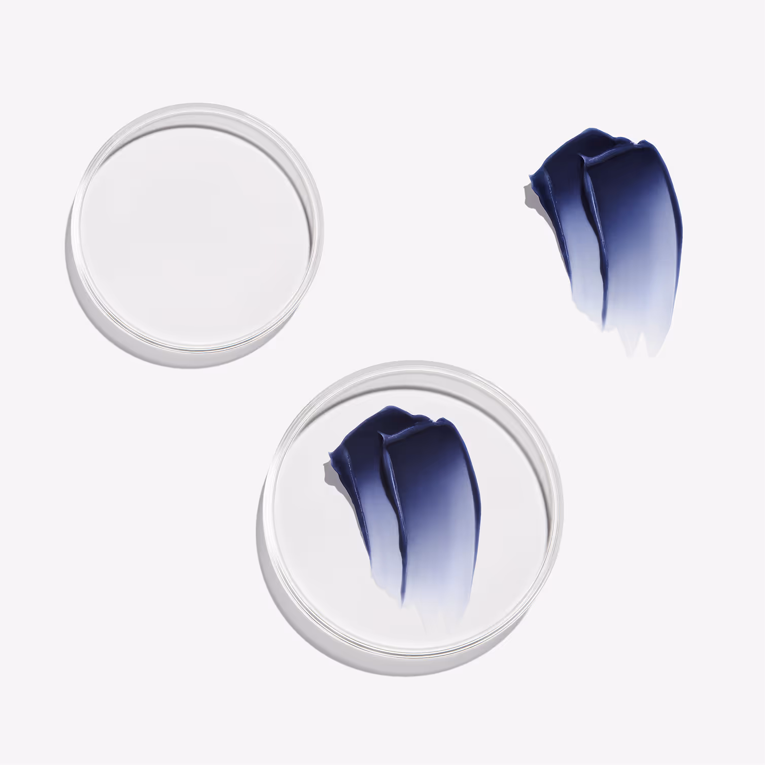 Transparent round containers with dark blue cream, one container open with cream nearby on white background.