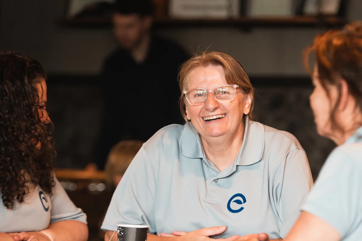 Team members in Ecobliss polo shirts laughing together at a wooden table