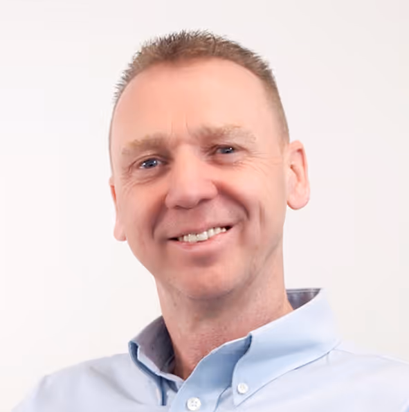 Smiling man with short hair wearing a light blue button-up shirt against a white background.