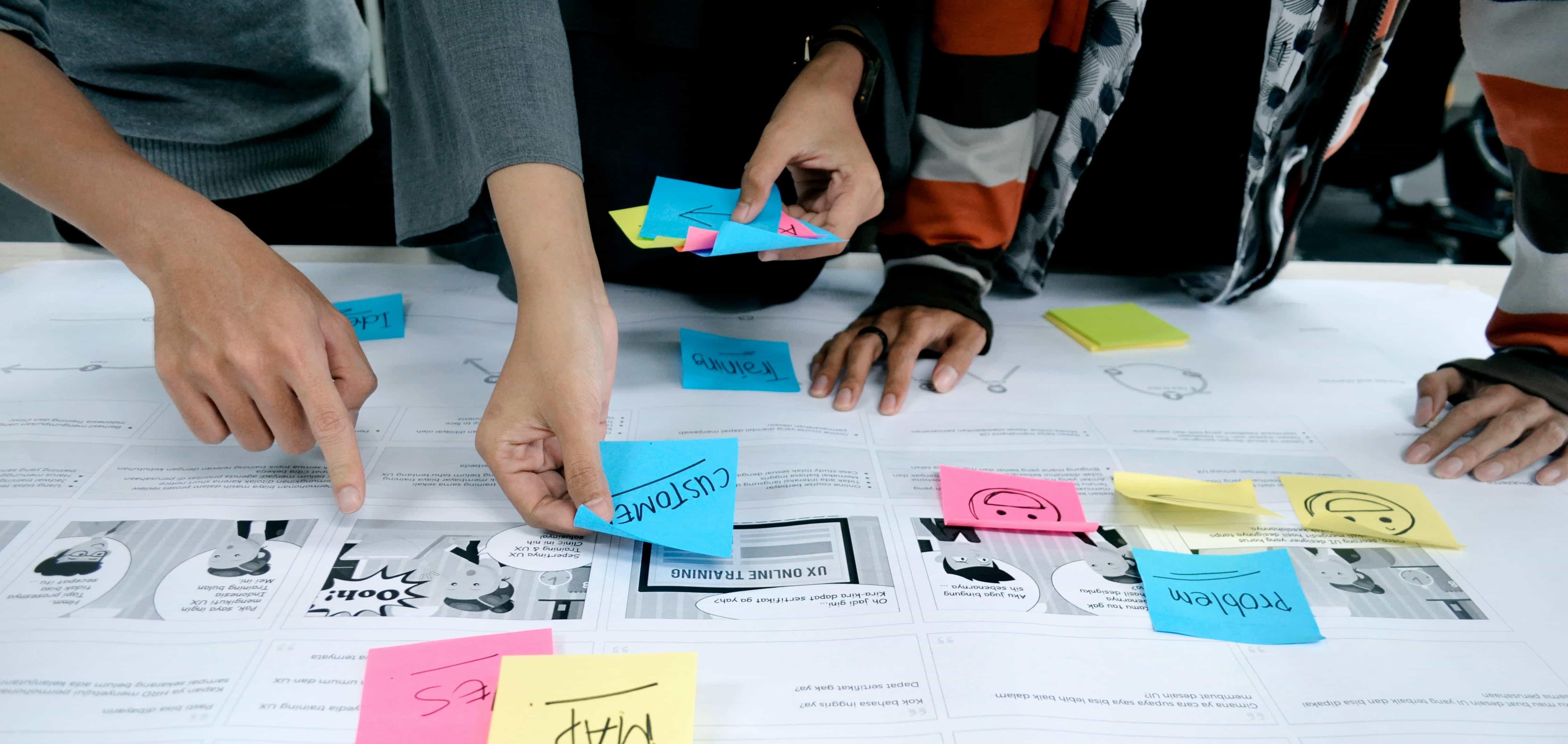Three individuals putting coloured post-it notes onto blueprint documents