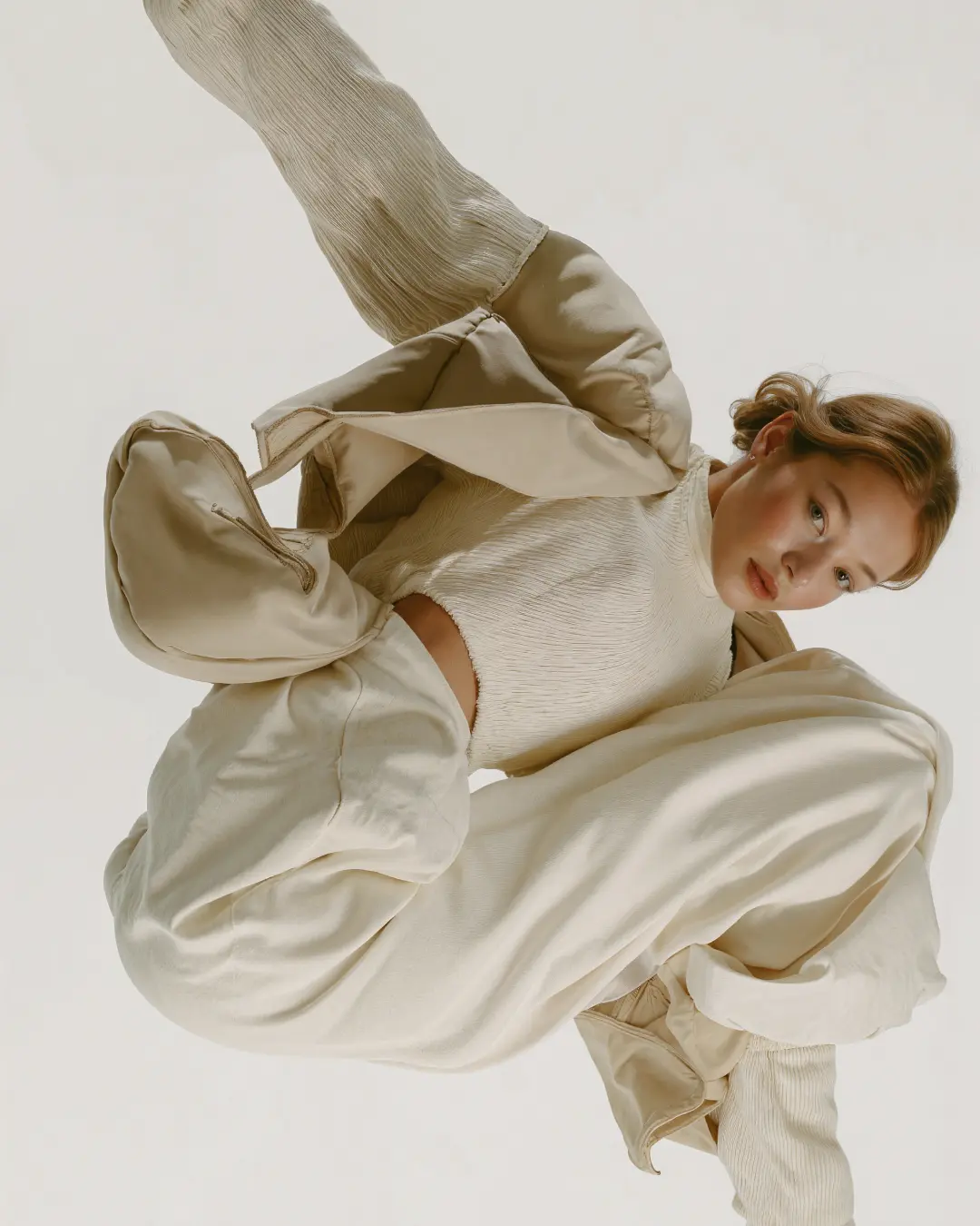 Porträt einer jungen Frau in beigefarbener, lockerer Kleidung vor weißem Hintergrund.