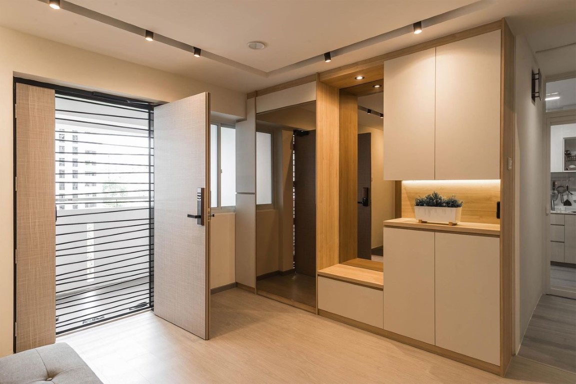 Open-entry foyer with a light-wood main door and digital lock, metal grille gate, built-in shoe cabinet and bench with warm under-cabinet lighting.