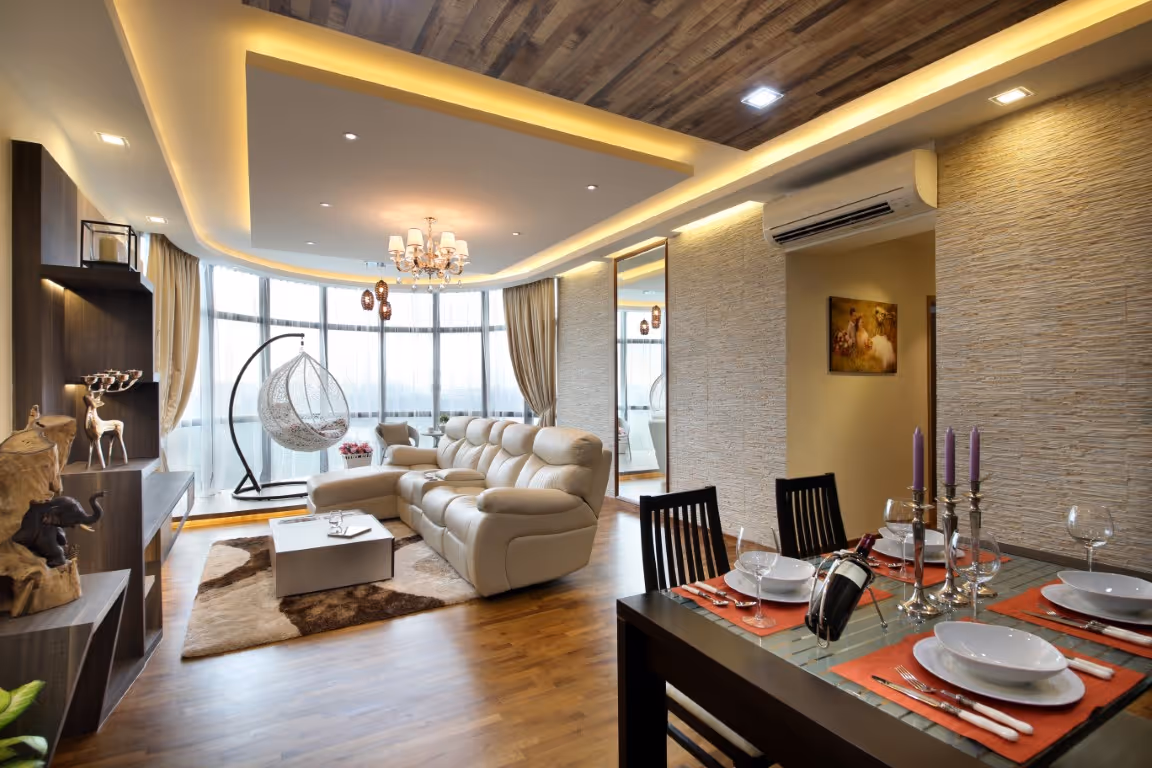 Open-plan living and dining room with warm-toned wooden plank flooring running throughout, cove lighting, textured feature wall, cream sectional sofa, and a formal dining set.
