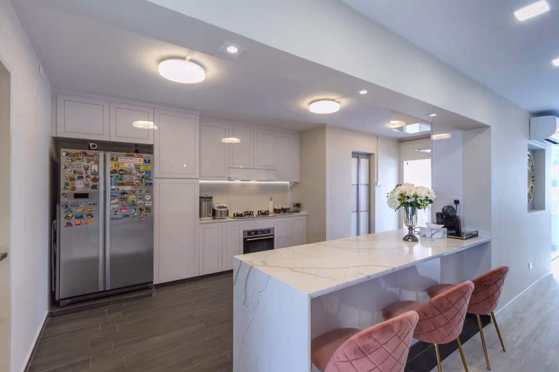 Bright modern kitchen with glossy white shaker cabinets, a stainless side-by-side fridge, and a marble-look engineered-stone waterfall peninsula with pink quilted bar stools.