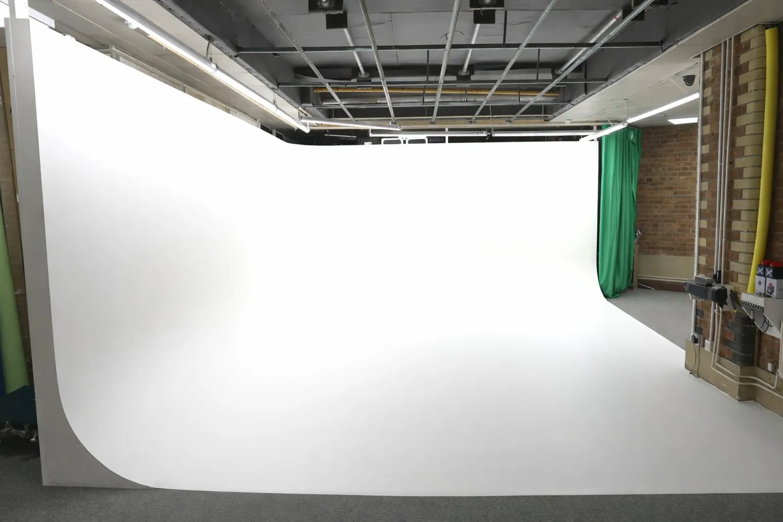 Empty infinity cove film and photography studio with large white cyclorama backdrop and green curtains on the side.