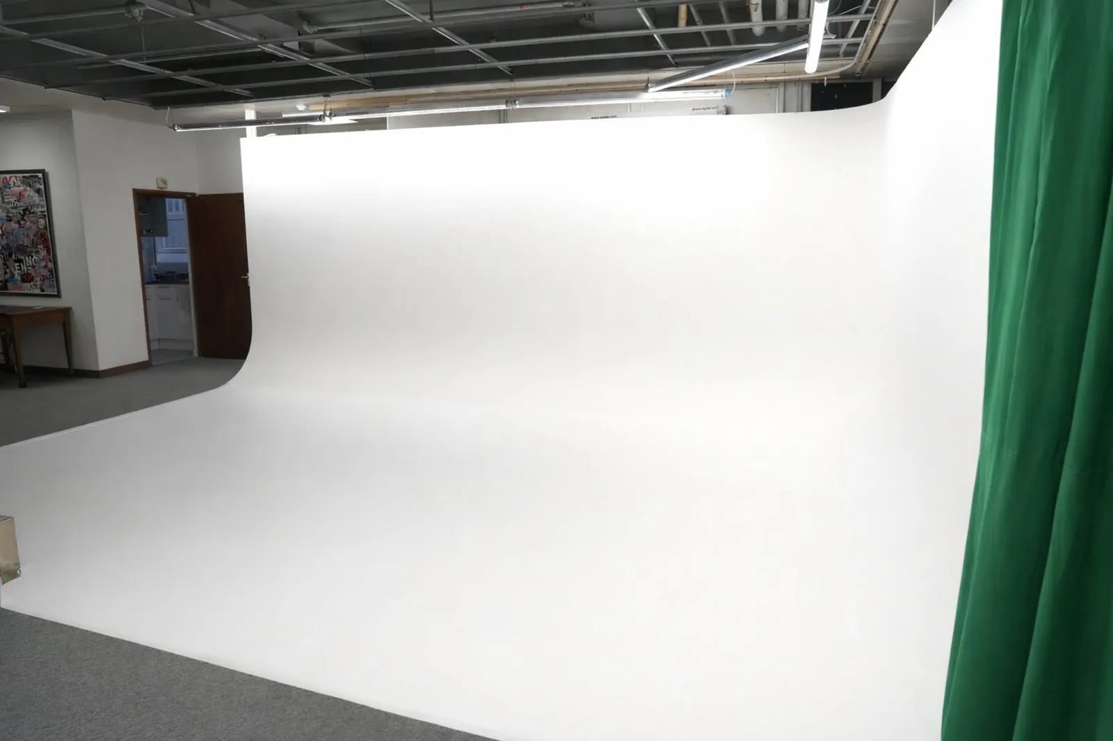 Empty infinity cove film and photography studio with a large white seamless cyclorama wall and a green curtain on the right.