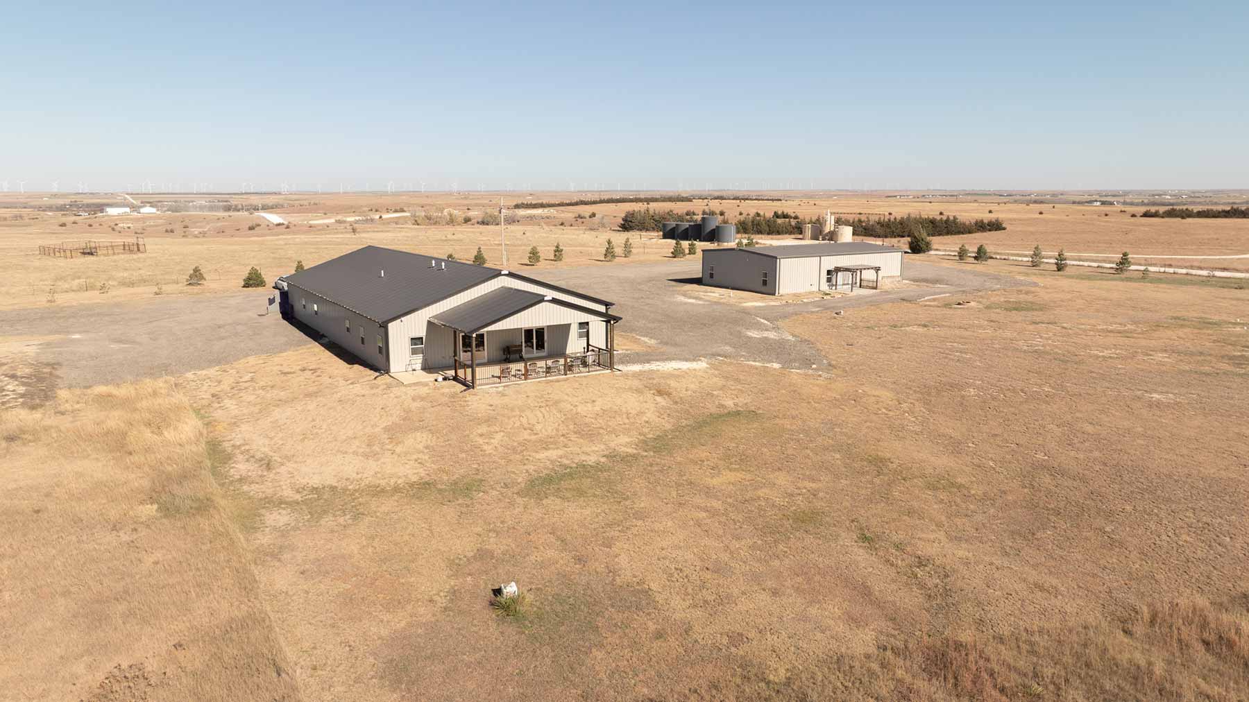 Aerial view of two gray industrial buildings on dry, grassy land under a clear sky.