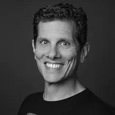 Black and white portrait of a smiling man with short curly hair against a dark background.