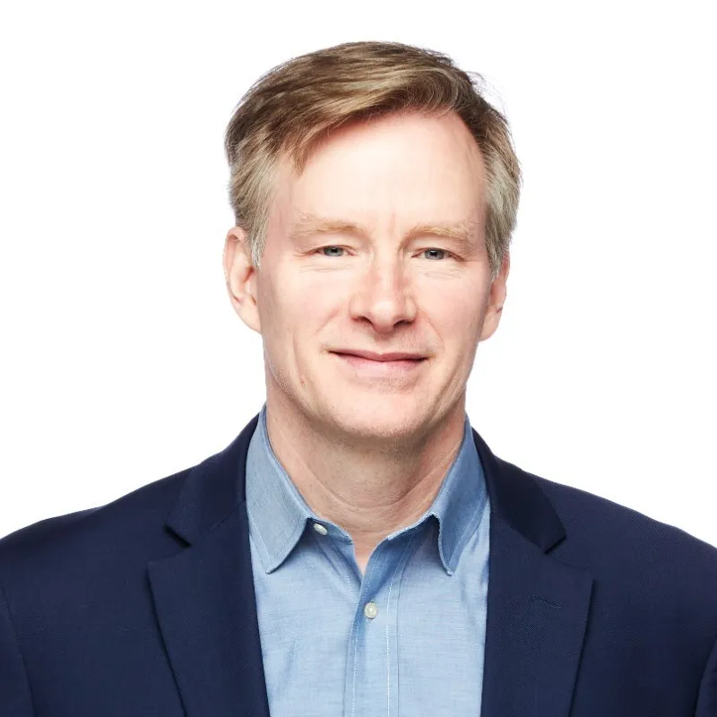 Middle-aged man with light brown hair wearing a blue dress shirt and navy blazer, smiling slightly.