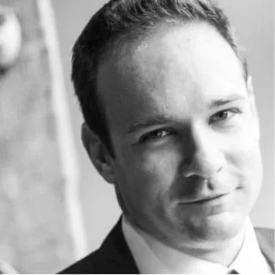 Black and white portrait of a man with short hair wearing a suit jacket and shirt, looking slightly to the side.