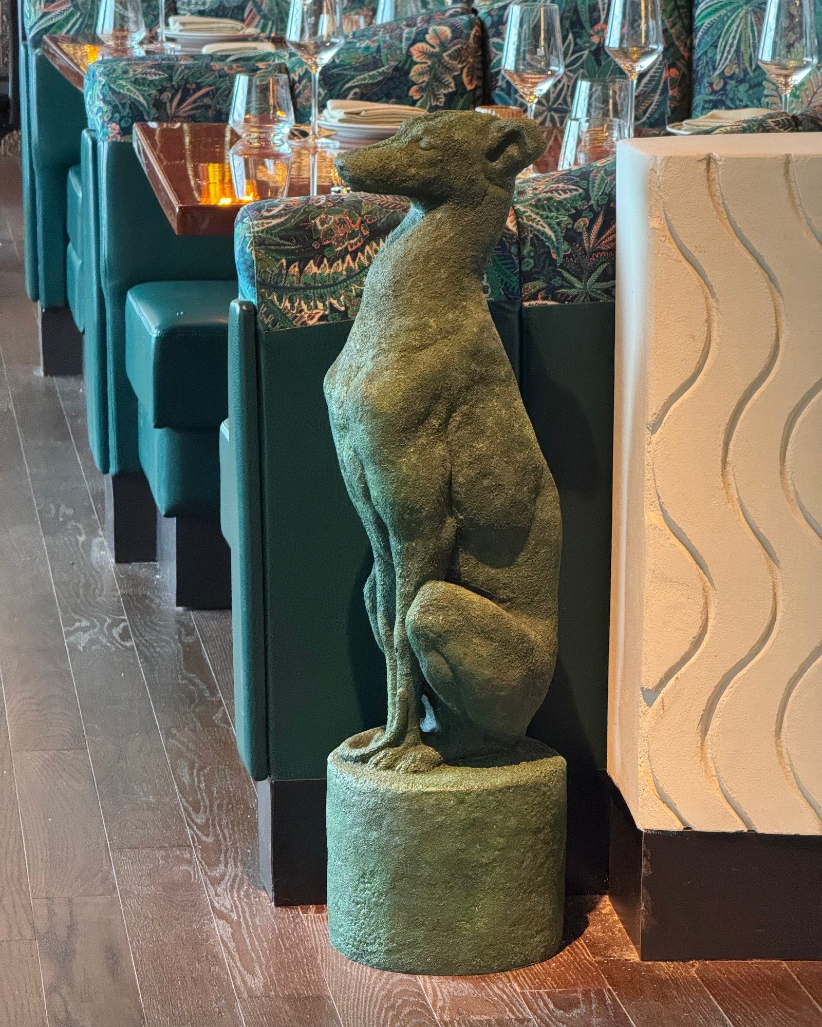 Patinated hound sculpture on a cylindrical plinth in a restaurant