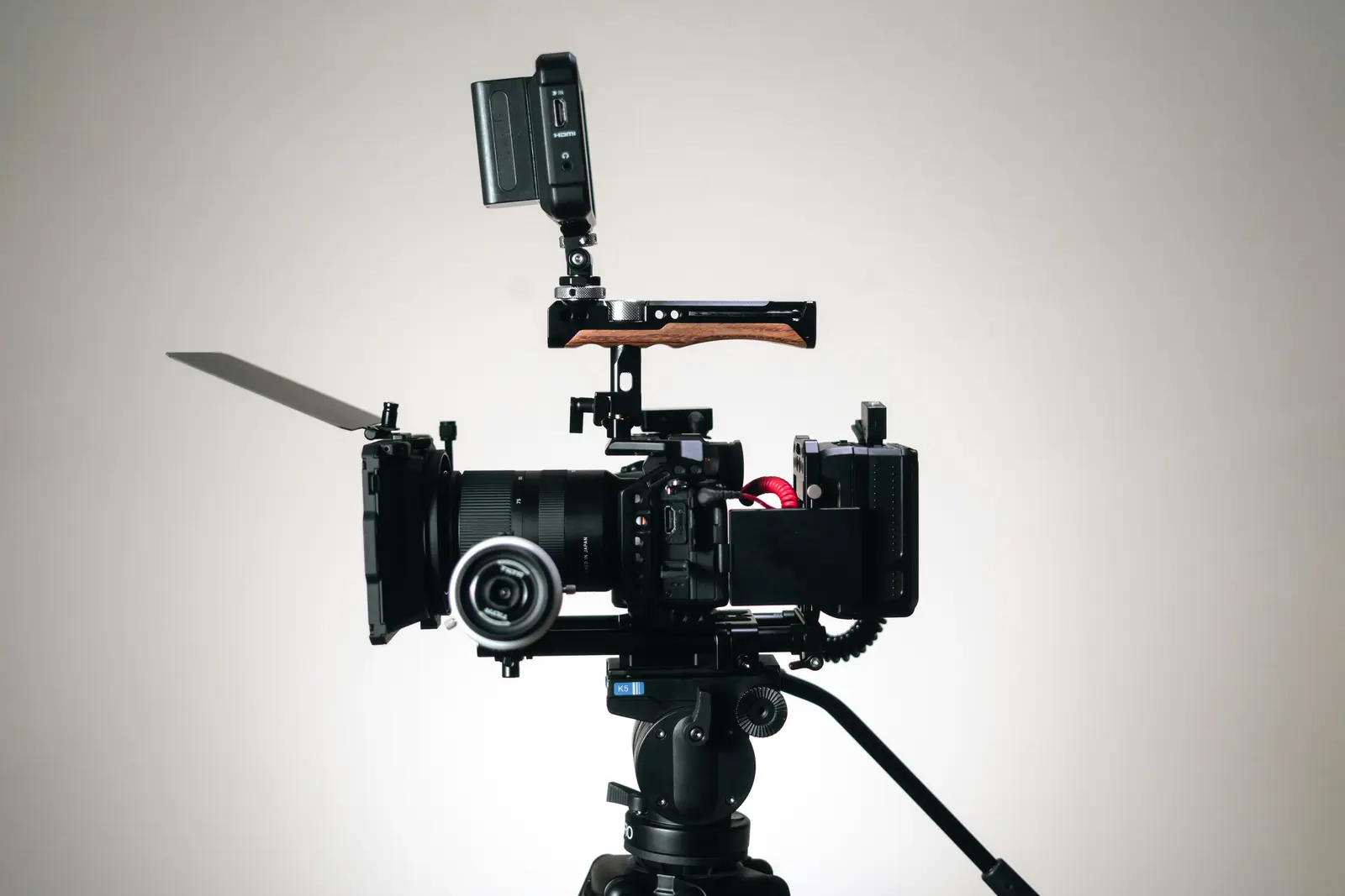 Cinema camera rig with top handle, matte box and monitor set up on a tripod against a plain studio background