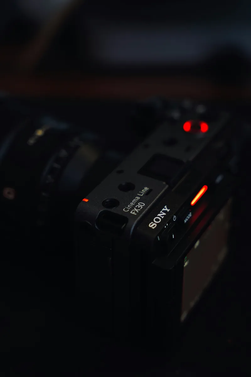 Close-up of the Sony FX30 top plate in a dark room, lit only by its red recording tally lights
