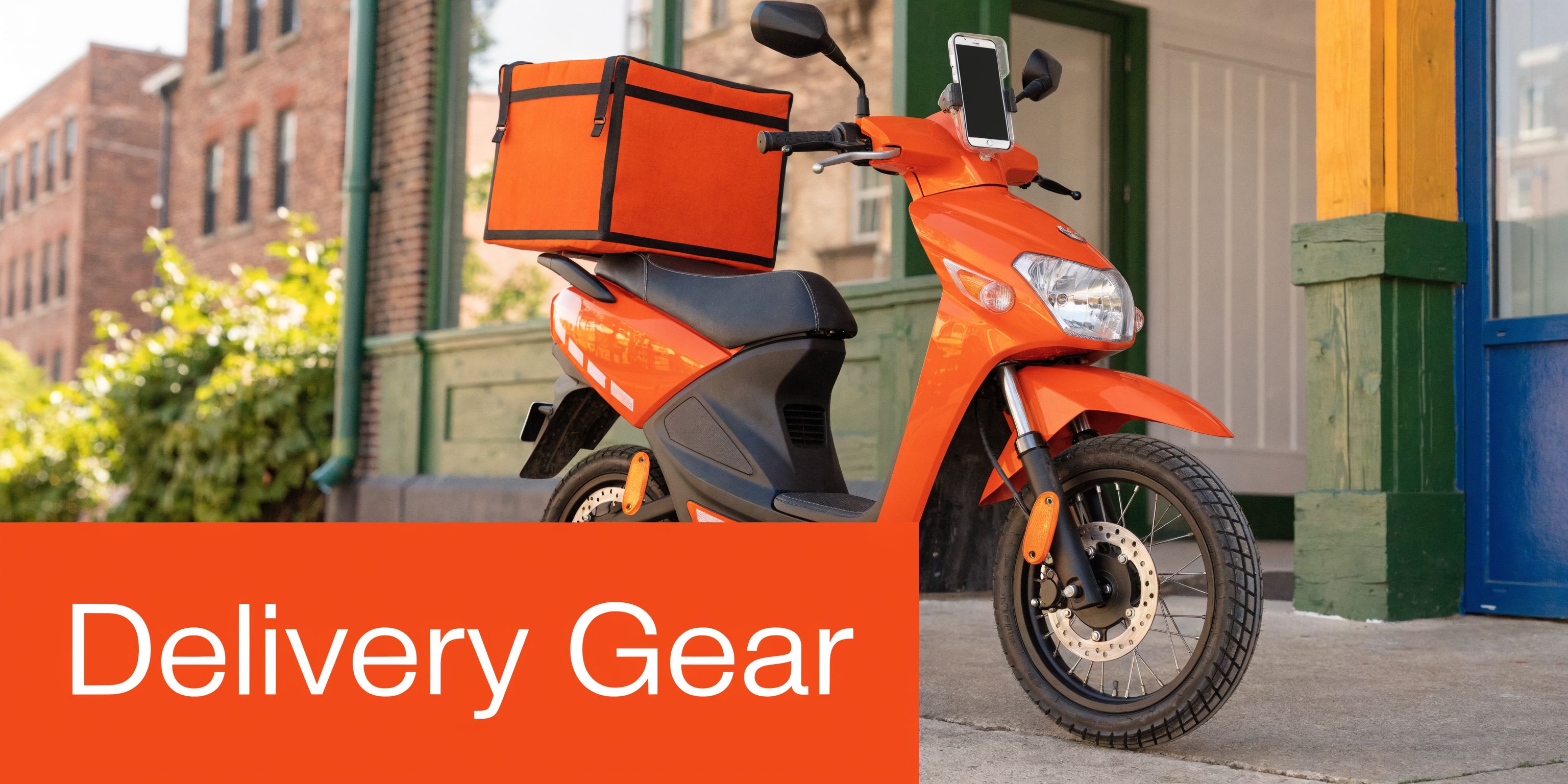 A bright orange electric scooter with a delivery box parked in front of a city building.
