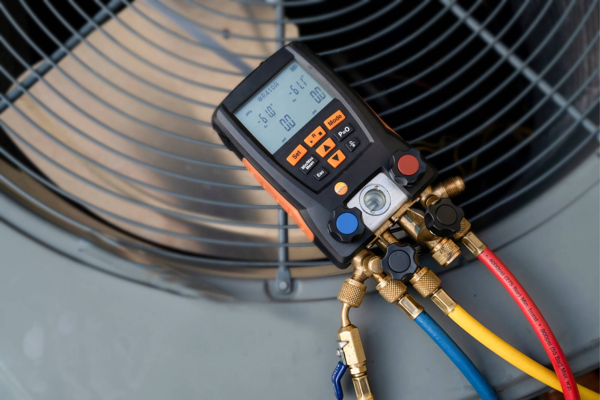 Digital HVAC manifold gauge set on air conditioning unit, displaying pressure readings, with colorful hoses attached.