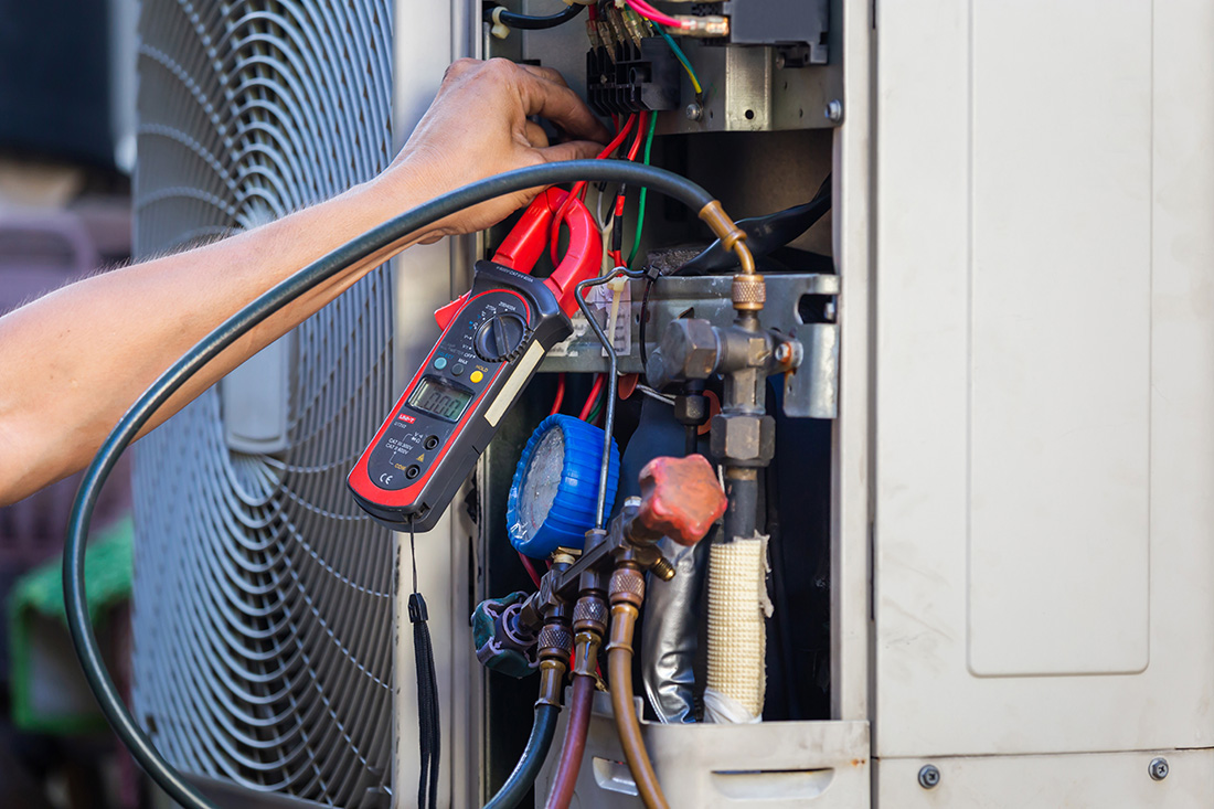 Person's hand working on HVAC unit with cables and gauges.