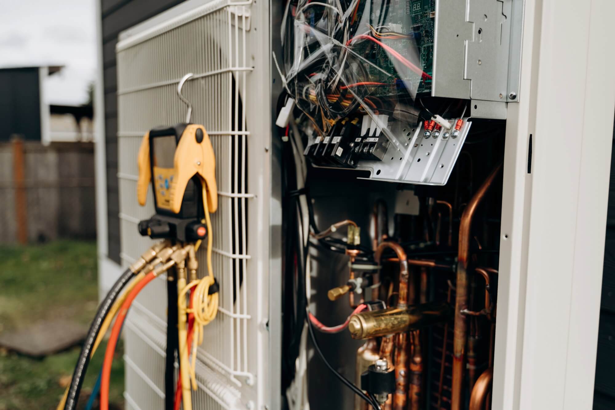 Air conditioning unit repair with exposed wiring and pressure gauges outdoors.