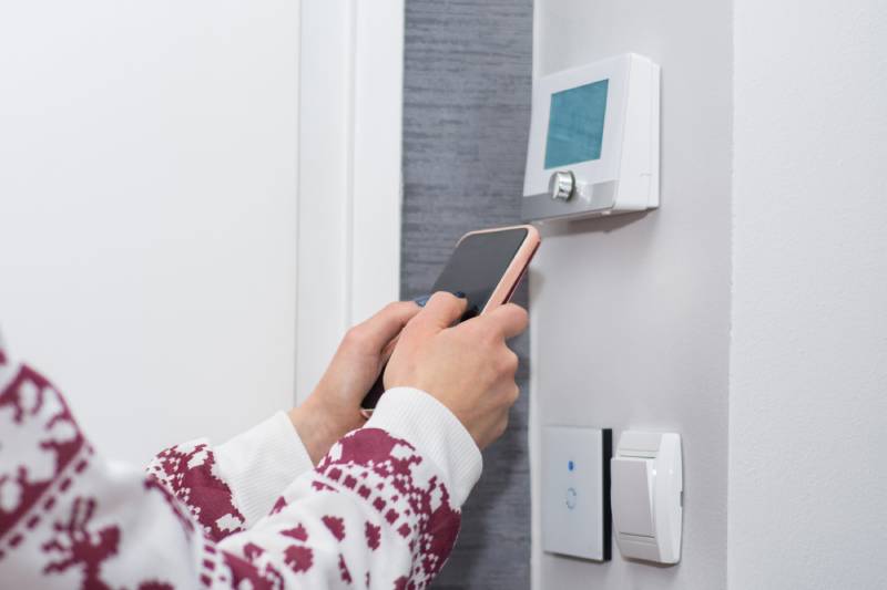 Person adjusting smart thermostat with phone.