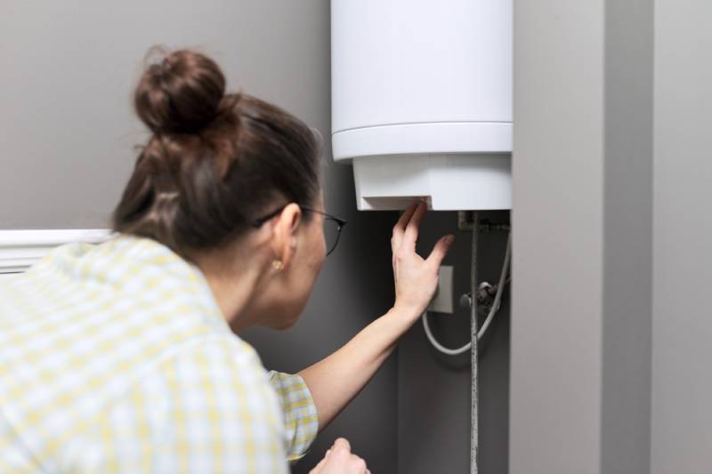 Woman checking water heater pilot light.