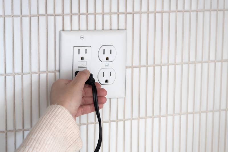 Plugging cable into GFCI outlet on tiled wall.